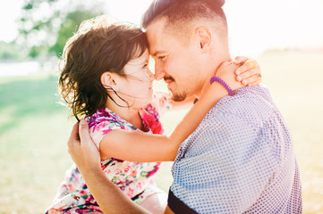 Young handsome father holding, hugging her little cute daughter outdoor in summer park. Fatherhood concept. Dad playing with cheerful child girl. Family having fun in park. Parent embracing baby.