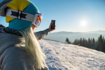 Woman snowboarder relaxing after snowboarding, taking photos of winter nature in the mountains...