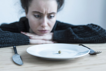 Young woman with anorexia and depression sitting opposite the kitchen table. Sadness, nostlagic, depression. disgust for eating. Mental problems of young people. - obrazy, fototapety, plakaty