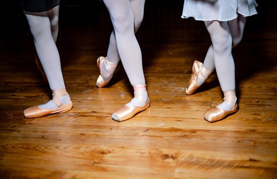 Detail of ballet dancers' feet of three girls standing in special position on wooden floor. Ballerinas legs in pointes. Close-up.