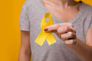 Woman with yellow ribbon on color background. Cancer awareness concept