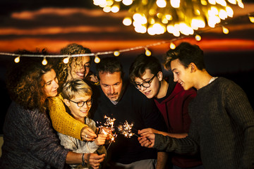 Group of friends celebrate together christmas night or new year eve or birthday or party like anniversary using sparkles light and having a lot of fun in friendship - mixed generations
