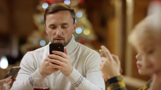 Man, woman and litle boy surfing the Internet on smartphones by Xmas full table, close up shot