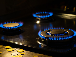 Burning gas, gas stove burner with coins on the fore ground, hob in kitchen