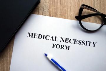 Medical necessity form, pen and glasses on desk