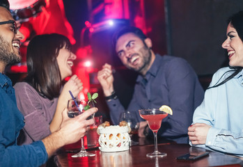 Group of happy friends drinking cocktails inside a jazz cocktail bar - Millennial young people having fun and laughing together in american pub - Friendship, nightlife and youth lifestyle holidays
