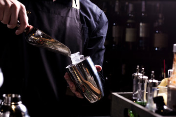 Bartender making refreshing coctail on a bar background. Dark moody style. Ice in tha glass