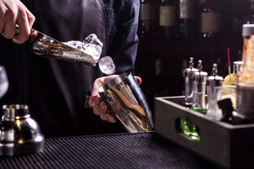 Bartender making refreshing coctail on a bar background. Dark moody style. Ice in tha glass
