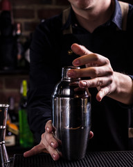 Bartender making refreshing coctail on a bar background. Dark moody style. Ice in tha glass