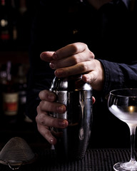 Bartender making refreshing coctail on a bar background. Dark moody style. Ice in tha glass