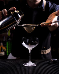 Bartender making refreshing coctail on a bar background. Dark moody style. Ice in tha glass