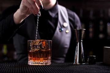 Bartender making refreshing coctail on a bar background. Dark moody style. Ice in tha glass