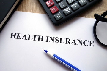 Health insurance document, calculator, pen and glasses on   desk