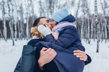 Fototapeta na wymiar Guy carrying his girlfriend on hands and kissing in winter forest. People having fun outdoors