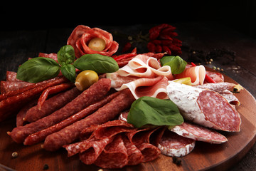 Food tray with delicious salami, pieces of sliced prosciutto crudo, sausage and basil. Meat platter with selection