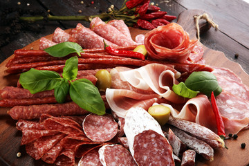 Food tray with delicious salami, pieces of sliced prosciutto crudo, sausage and basil. Meat platter with selection