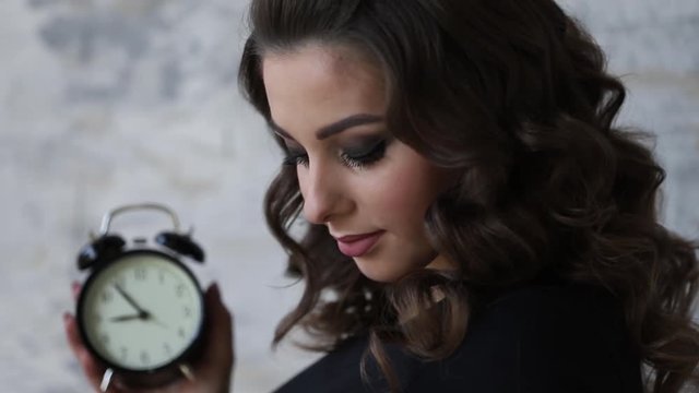 Beautiful pregnant woman in black bodysuit. She hold the clock in hands symbolic hinting at the remanining time befour the baby in born. Woman put her hand on belly. close up