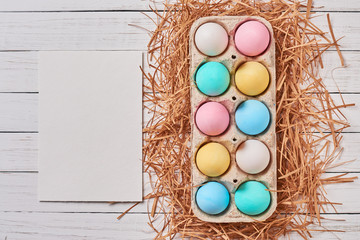 Colorful easter eggs in paper tray and a white empty sheet top view
