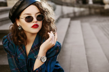 Outdoor fashion portrait of young beautiful fashionable girl wearing trendy sunglasses, wrist...
