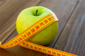 Green apple with measuring tape on wooden background. Apples and sewing tape measure on a wooden table. To lose weight and eat a low calorie apple to lose weight