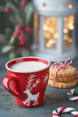 Closeup on red cup of milk with Christmas deer design, cookies, Xmas lights in lantern and berry