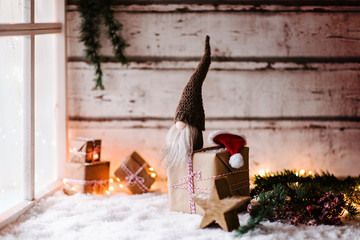 Kleiner Wichtel sitzt auf Geschenken vor einem Fenster und wartet mit seiner weihnachtsmütze auf...