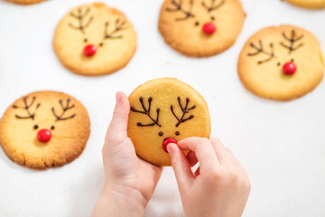 Child decorates homemade cookies with candy and chocolate icing.  Christmas deer cookies.
