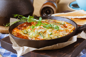 Tasty Breakfast Shakshuka in a Iron Pan. Fried eggs with tomatoes, onion, parsley, bread and herbs. Healthy Food