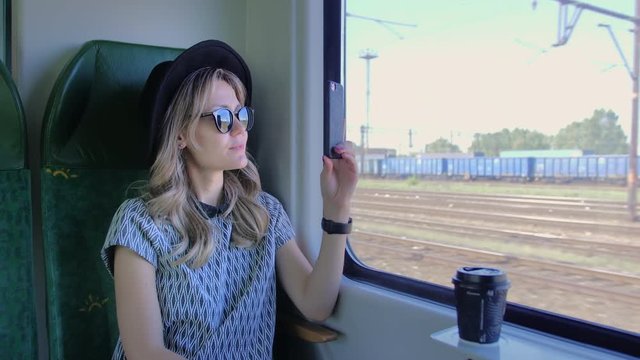 Caucasian girl in a hat travels in a train. Takes photos of nature on a mobile smartphone. Slow Motion.