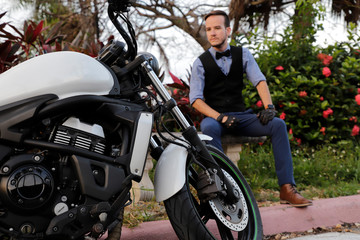 Fototapeta na wymiar Motorcycle. In the background guy model in a classic suit. Bow Tie and Vintage Motorcycle Leather Gloves.
