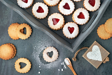 Top view of traditional Christmas Linzer cookies with strawberry jam in wooden tray on dark background