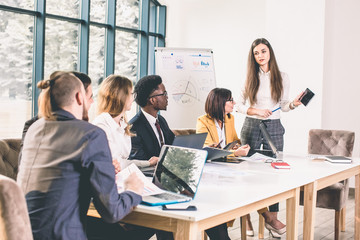 Making great decisions. Young beautiful woman gesturing and discussing something with smile while her coworkers listening to her sitting at the office table