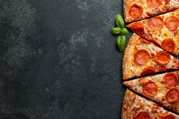 Cut into slices delicious fresh pizza with sausage pepperoni and cheese on a dark background. Top view with copy space for text. Pizza on the black concrete table. flat lay
