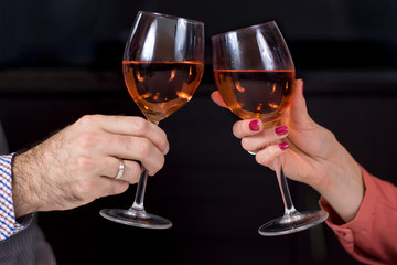 Dłonie kobiety i mężczyzny z kieliszkami do wina w dłoniach wznoszą toast. Kieliszki z winem na ciemnym tle.