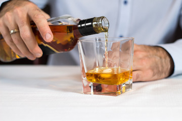 Męska dłoń nalewa whisky z butelki do szklanki z lodem. - obrazy, fototapety, plakaty