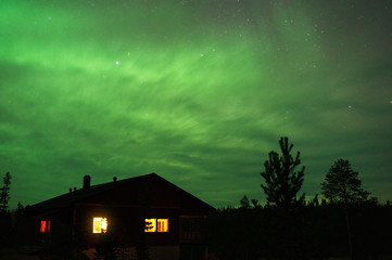 Night sky with Aurora Borealis above country house.