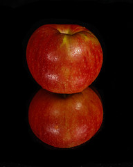 Red apple on mirror with black background.