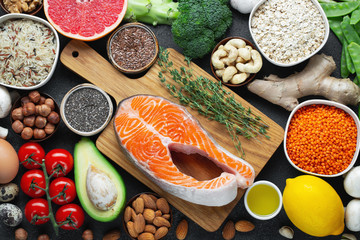 Healthy food clean eating selection: fish, fruit, nuts, vegetable, seeds, superfood, cereals, leaf vegetable on black concrete background. Flat lay