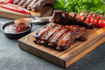 Closeup of pork ribs grilled with BBQ sauce and caramelized in honey. Tasty snack to beer on a wooden Board for filing on dark concrete background