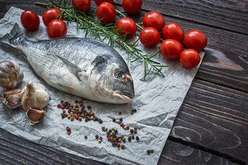 Raw dorado fish with garlic and tomatoes on rustic background. Sea bream or dorada fish. Top view, copy space