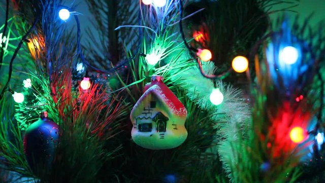 Illuminated New Year garland and toy house on pine-tree. Closeup 
