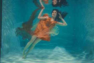 beautiful model girl swims underwater in orange dress and enjoys relaxation and lack of stress