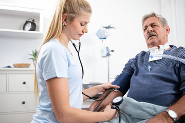 young pretty blonde nurse nurses an elderly patient in the hospital and measures his blood pressure with a cuff and prepares to inject with a syringe