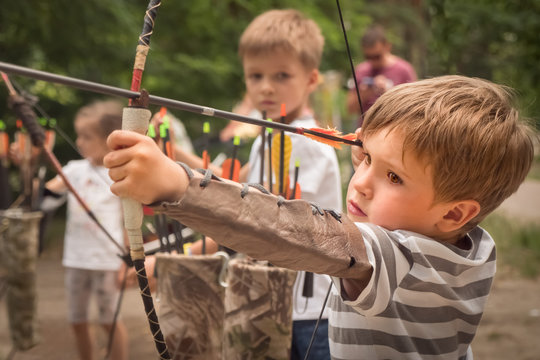 Boy with bow and arrow concentrated on target. Kid stared at target. Child directed arrow at a target. Bowman background. Children and sports. Physical training. Alternative schooling.