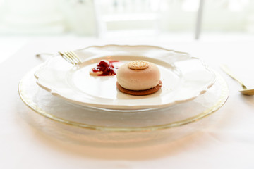 Ice cream dessert with biscuit and red fruit jam elegantly presented with golden cutlery and white background.