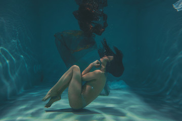beautiful girl in a transparent jumpsuit with rhinestones on the whole body swims underwater as a...