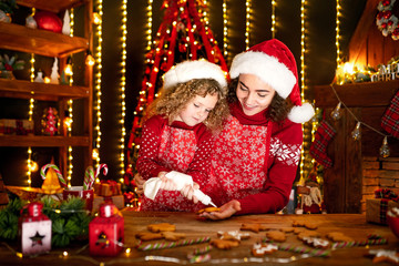 Merry Christmas and Happy Holidays. Family preparation holiday food. Cheerful cute curly little girl and her older sister in santas hats cooking Christmas cookies.