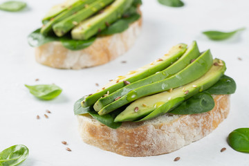 Two ciabatta toast with sliced avocado olive oil, spinach and flax and sesame seeds. Healthy vegetarian Breakfast on white background