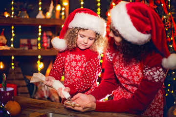 Merry Christmas and Happy Holidays. Family preparation holiday food. Cheerful cute curly little girl and her older sister in santas hats cooking Christmas cookies.