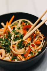 Chopsticks and delicious salad with vegetables shrimps in black plate, Asian cuisine